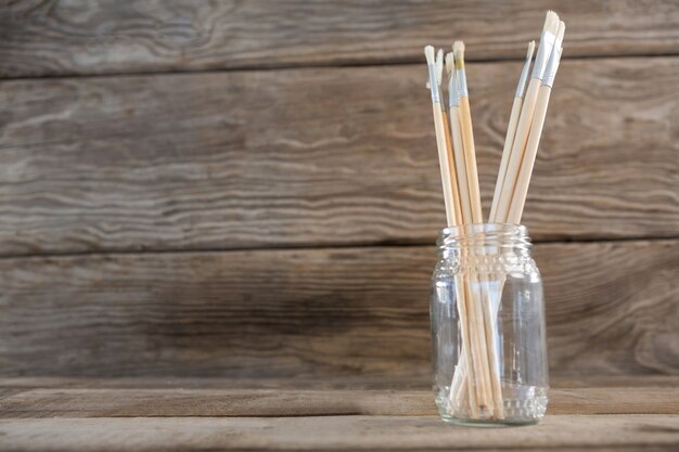 Various paintbrush in a glass jar on wood surface