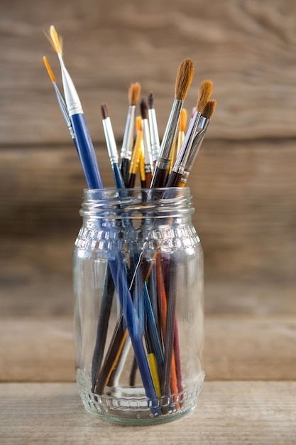 Various paintbrush in a glass jar on wooden surface