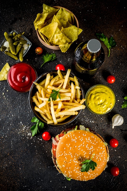 Various party food, Hamburgers, French fries, potato chips, pickled cucumbers, onions, tomatoes and cold beer bottles, rusty black concrete table