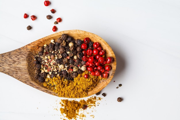 Various peppers and spices on a wooden spoon