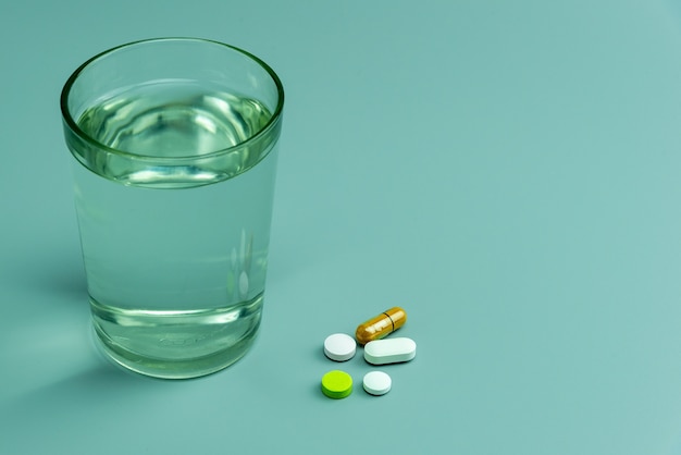 Various pills and glass of water on gray background