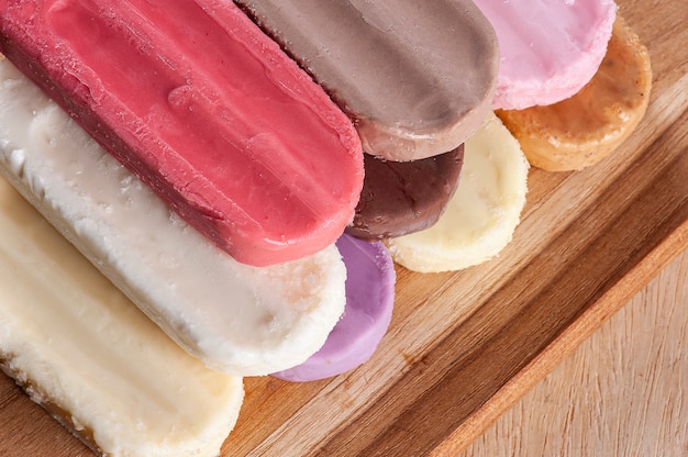 Photo various popsicles are placed on the wooden board background. variety of flavors and colors.