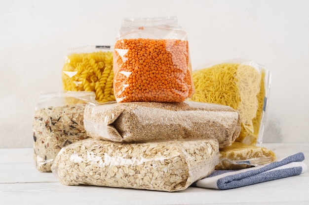 Various raw groats, cereal grains and pasta in transparent plastic bags on a kitchen table. Ingredients for cooking.