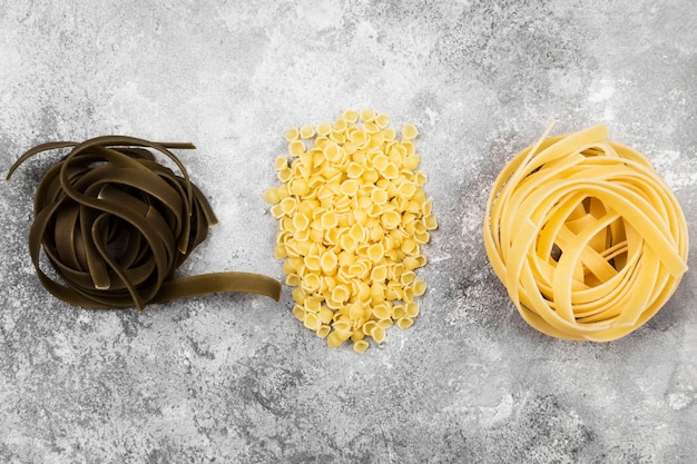 灰色の背景にさまざまな生パスタ。上面図。食品の背景