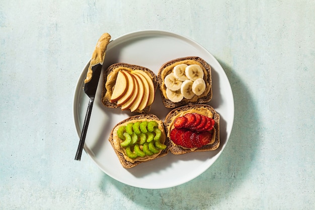 Vari panini con burro di arachidi e fragole, sedano, banana e mela su un piatto sul tavolo. perfetta colazione mattutina