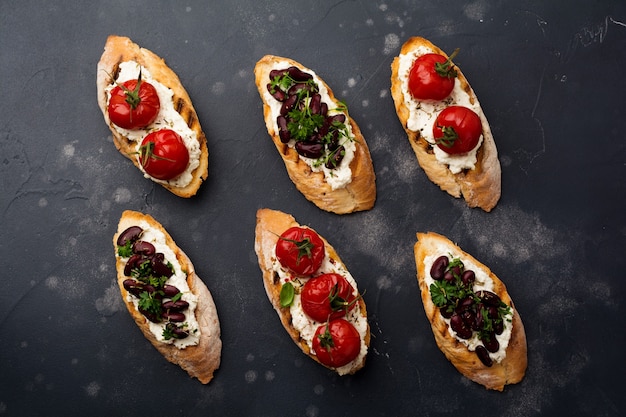 Various sandwiches with red beans, baked cherry tomatoes, garlic, olive oil and curd cheese on dark surface