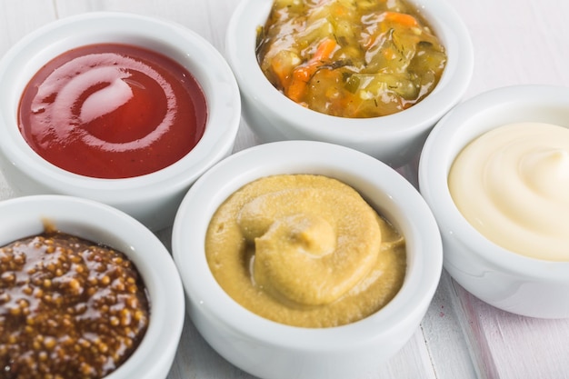 Various sauces in jars on wooden background, top view