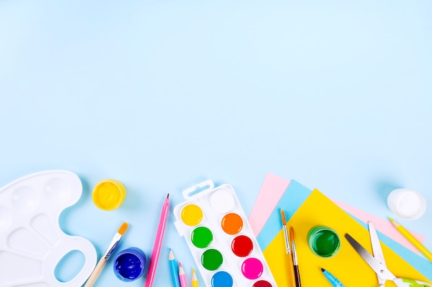 Various school office and painting supplies on blue background