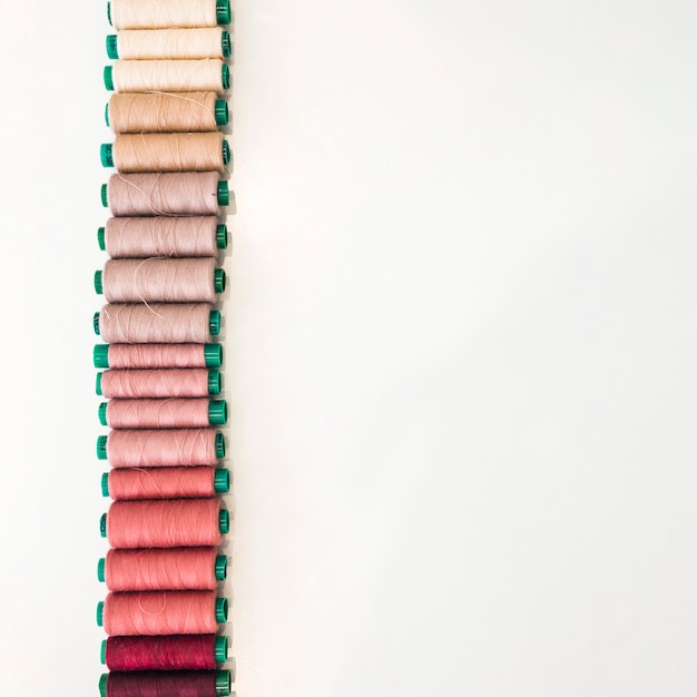 Various shade of spools arranged in a row on white backdrop