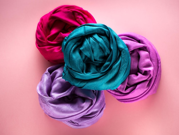Various silk and woolen scarves on a pink background top view