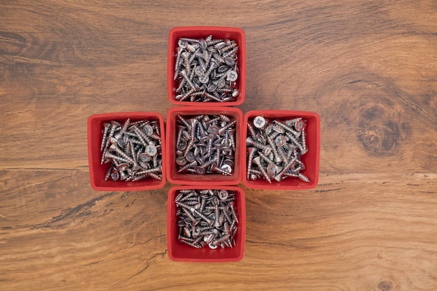 Various size and shape of screws selection in red plastic tray box on a wooden background Top view