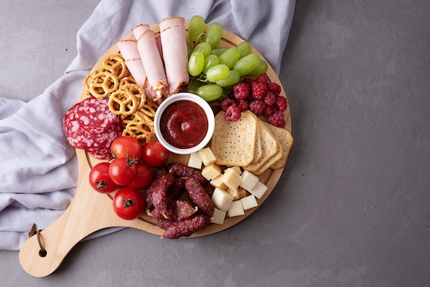 Various snacks on a round charcuterie board on a gray background, party a appetizer, close-up.