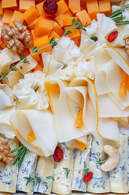 Vari tipi di formaggio disposti su un piatto, decorati con frutti di bosco, noci ed erbe aromatiche, vista dall'alto