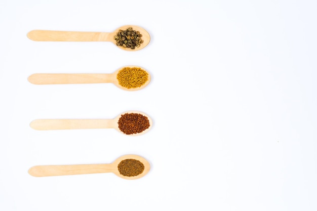 Various spice seeds in wooden spoons on a white background Seeds of beet mustard lettuce arugula on a white background Place for an inscription View from above