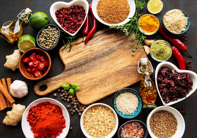 Various spices in a bowls and empty cutting board on black concrete table. Top view copy space.