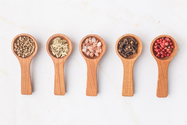 Various spices and green herbs in wooden spoons on white table high quality photo