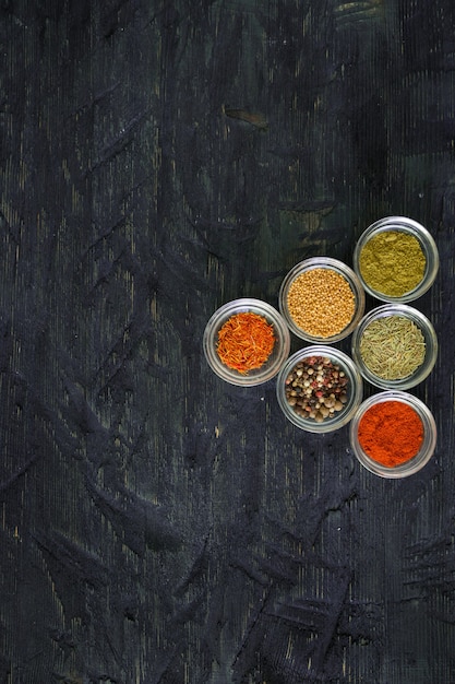 Various spices and herbs in a transparent bowl on black wooden background, top view with copy text.