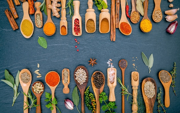 Various of spices and herbs in wooden spoons on the black stone.