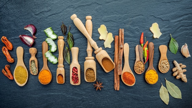 Various of spices and herbs in wooden spoons on the black stone.