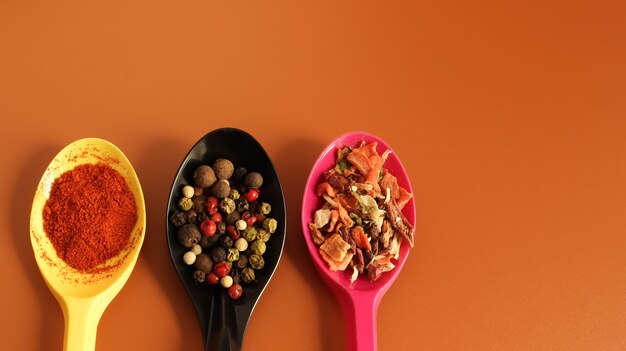 Various spices in plastic spoons on a brown background. Copy space. A mixture of peppers, red smoked paprika, seasoning twelve vegetables.