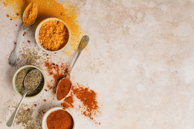 Various spices and seasonings: turmeric, paprika and provencal herbs on light brown stone background. Cooking background and copy space for text, top view.