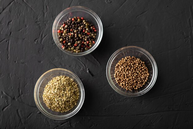 Various spices in three containers Pepper coriander oregano Dark background Closeup