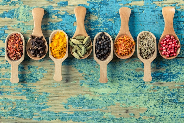 Various spices in wooden spoons on wooden background