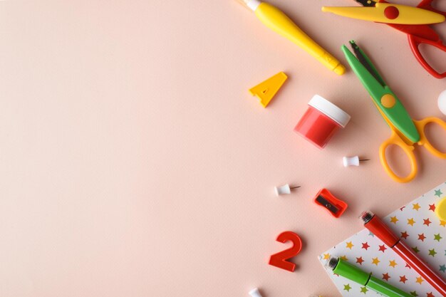 Vari elementi di cancelleria di colore rosso giallo e verde sono al centro su sfondo beige ritorno a scuola spazio per la copia posizione piatta vista dall'alto