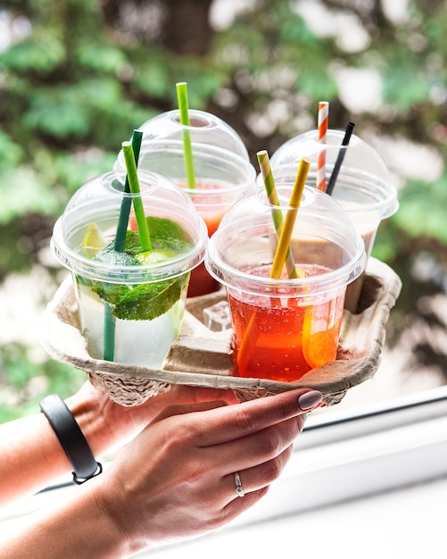 Various summer cold drinks and cocktails in a paper holder in women's hands