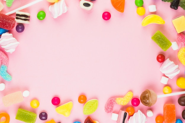 Foto varie caramelle dolci che formano struttura su fondo rosa