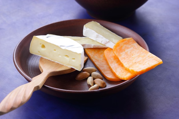 Various types of cheese composition on a blue background closeup Cheeses with nuts and a wooden spatula on a clay plate