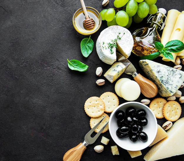 Various types of cheese, grapes, honey and snacks on a black concrete surface