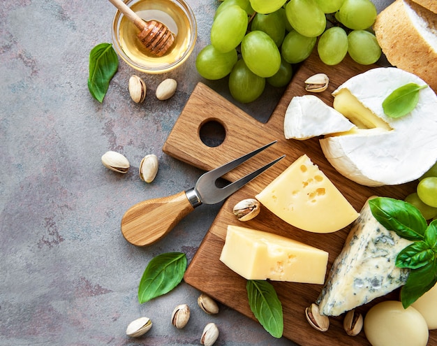 Vari tipi di formaggio, uva e snack su una superficie di cemento grigio