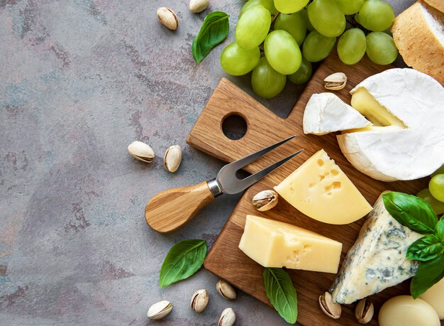 灰色のコンクリートのテーブルにさまざまな種類のチーズ、ブドウ、軽食