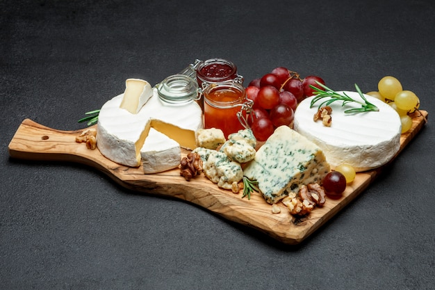 Various types of cheese and jam on wooden cutting board