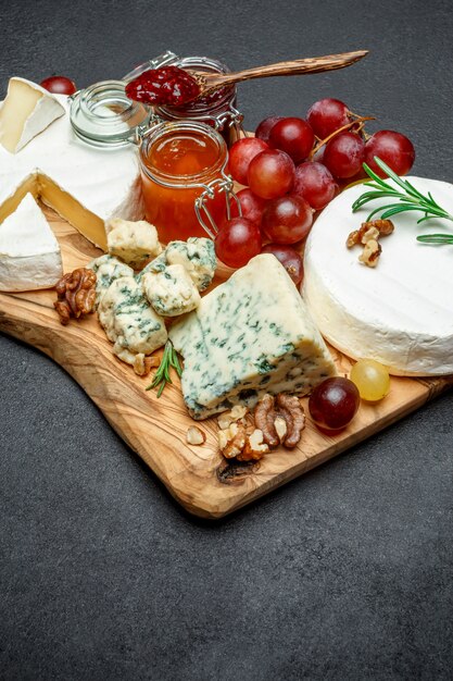 Various types of cheese and jam on wooden cutting board