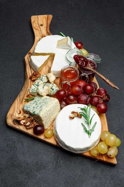 Various types of cheese and jam on wooden cutting board