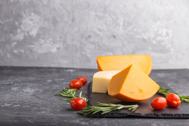 Various types of cheese with tomatoes on black slate board on black background