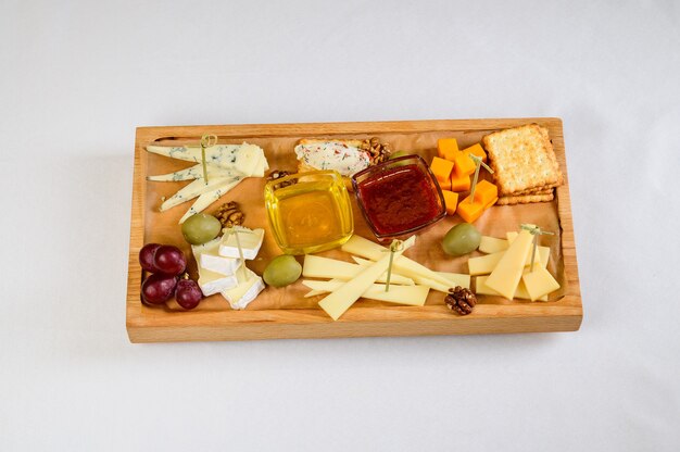 Various types of cheese on wooden cutting board, top view.