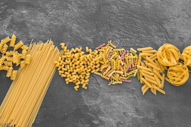 Various types of pasta on dark background from above