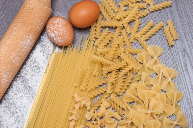 Various types or raw Italian pasta on the wooden background and ingredients for pasta. Top