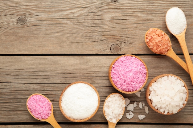 Various types of spa sea salt in wooden spoons on grey wooden surface