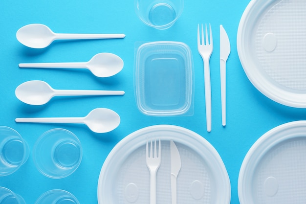 Various white plastic disposable tableware on blue surface. Creative flat lay.