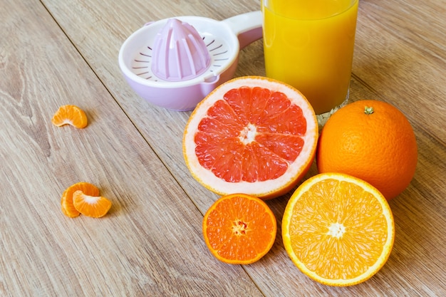 다양한 전체 및 절단 감귤류 과일 수동 리머와 나무 테이블에 오렌지 주스 한 잔