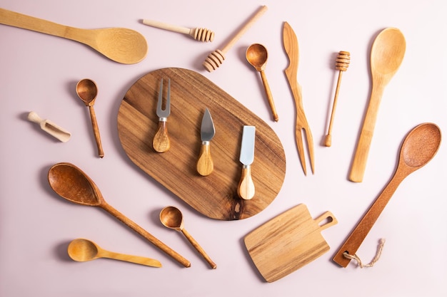 Various wooden and bamboo kitchen utensils are laid out on a pastel background top view flat lay