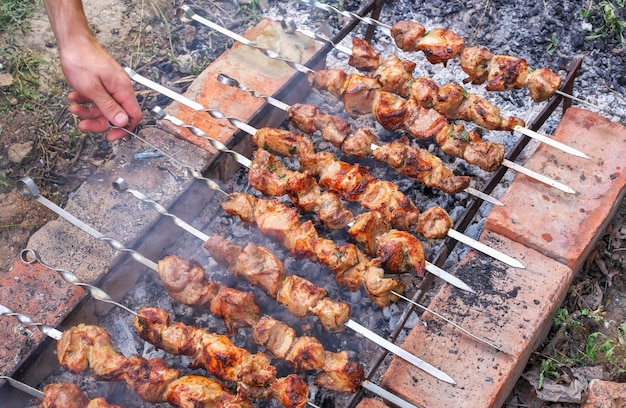 Varkenskebabs op de grill koken. de hand van de mens draait kebabs om op een grill voor een betere bereidingskwaliteit