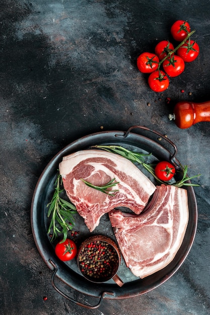 Varkenskotelet op een bot vers rauw vlees met kruiden en rozemarijn verticale afbeelding bovenaanzicht plaats voor tekst