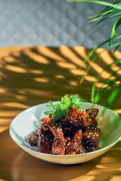 Varkensribbetjes in zoetzure saus met koriander, sesamzaadjes en Sichuanpeper in een witte kom. Chinese keuken