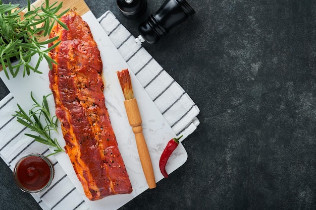 Varkensribbetjes Rauw vlees Rauwe varkensribbetjes in marinade met kruiden rozemarijn tomatensaus en knoflook op witte marmeren stand op zwarte stenen tafel achtergrond Barbecue concept bovenaanzicht Mock up