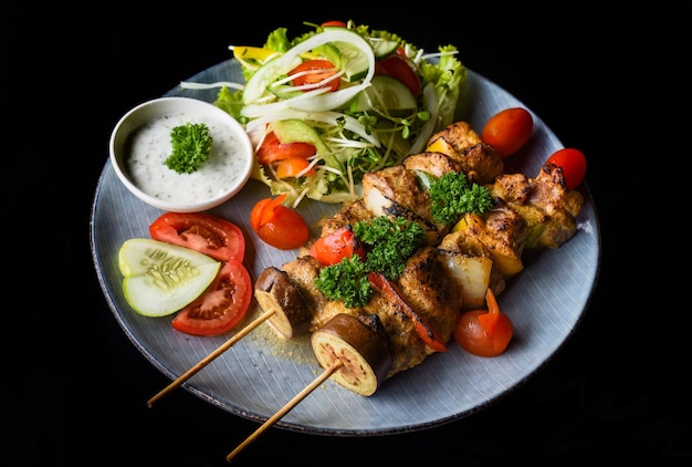 Varkensspiesjes met gegrilde groenten geserveerd met salade op zwarte achtergrond zijaanzicht